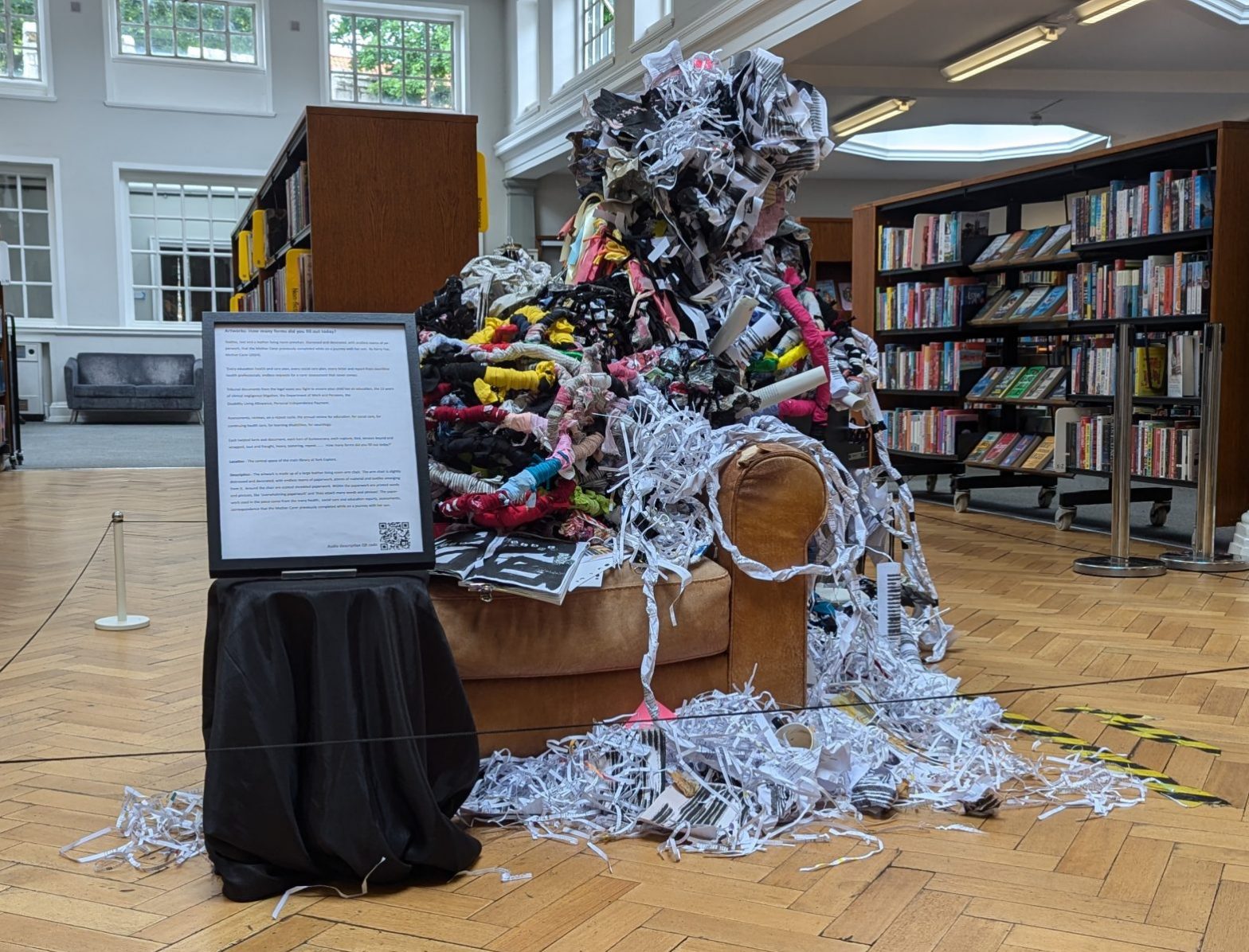 The artwork is made up of a large leather living room arm chair. The arm chair is slightly distressed and decorated, with endless reams of paperwork, pieces of material and textiles emerging from it. Around the chair are scatted shredded paperwork. Within the paperwork are printed words and phrases, like ‘overwhelming paperwork’ and ‘they attach many words and phrases’. The paper-work used in the piece come from the many health, social care and education reports, assessments, correspondence that the Mother Carer previously completed while on a journey with her son.